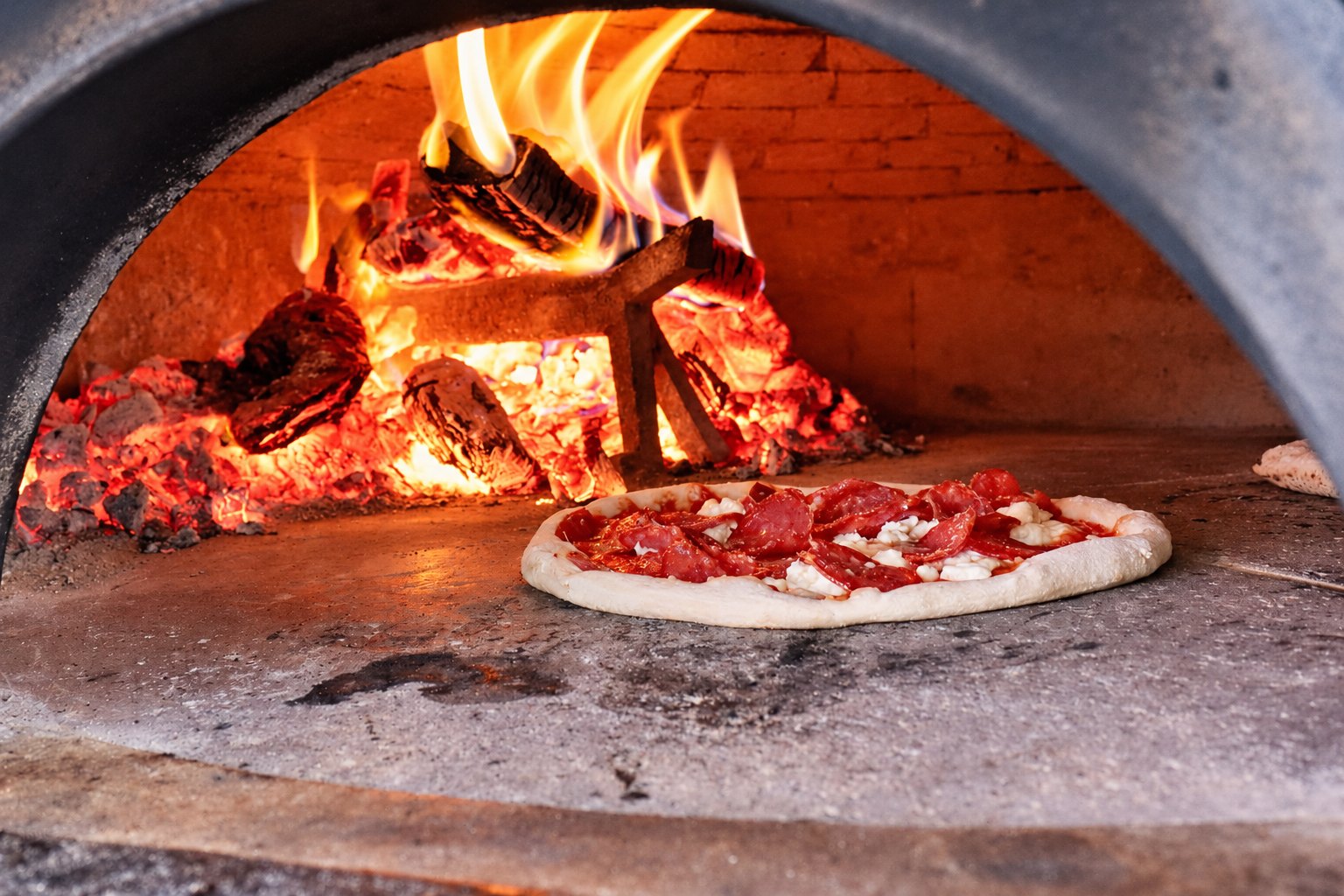 Pizza baking beside the flames in the wood-burning oven